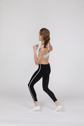Vista posterior de una jovencita en ropa deportiva dando un paso adelante mientras aprieta los puños