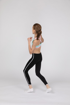 Back view of a teen girl in sportswear stepping forward while clenching fists