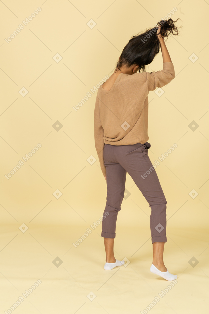 Vista traseira de três quartos de uma jovem de pele escura agarrando seu cabelo