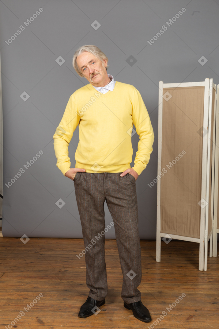 Вид спереди серьезного старика, засовывающего руки в карманы, глядя в камеру