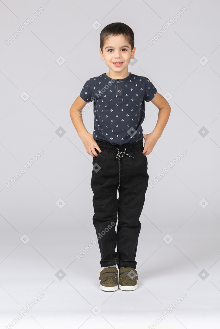 Front view of a happy boy standing with hands on hips and looking at camera