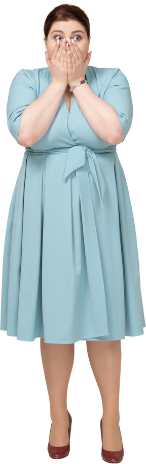 Vista frontale di una donna scioccata in abito blu che copre la bocca con le mani
