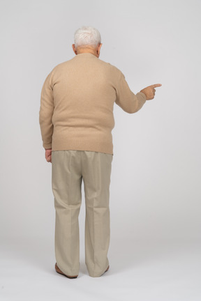 Rear view of an old man in casual clothes pointing down
