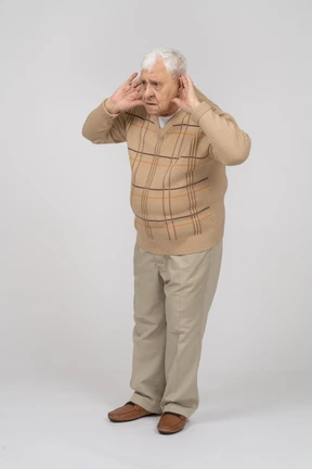 Vista frontal de un anciano con ropa informal sostiene las manos cerca de las orejas