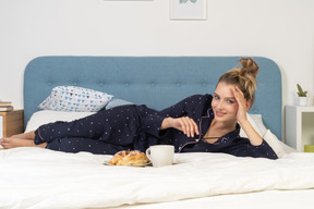 Vue de face d'une pose au lit jeune femme prenant son petit déjeuner