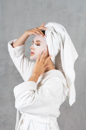 Vista lateral de una mujer en bata de baño que ajusta la máscara facial