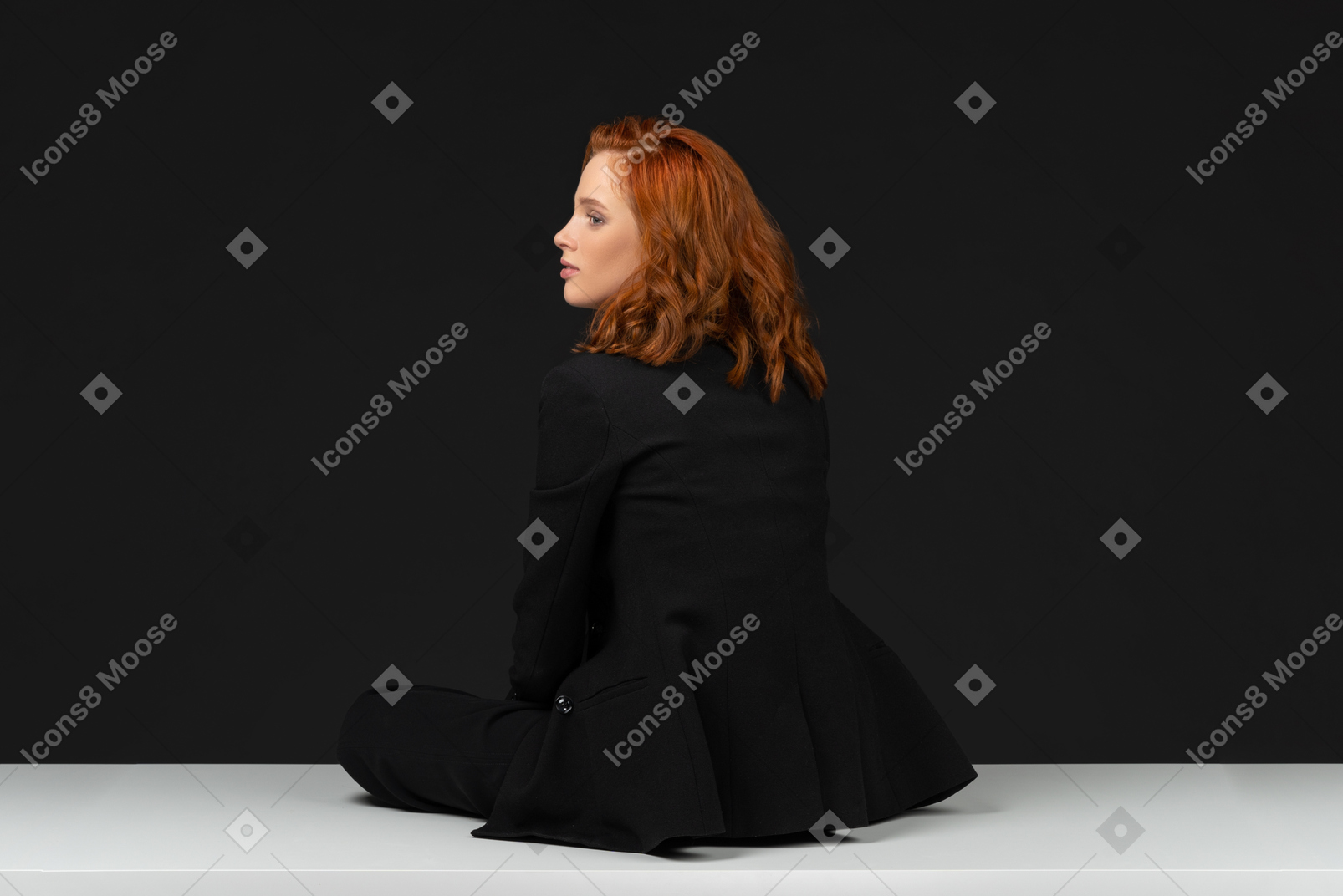 A back side view of the beautiful young woman dressed in black and sitting on the white table