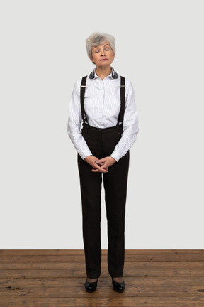 Front view of an old displeased female in office clothes grimacing and holding hands together