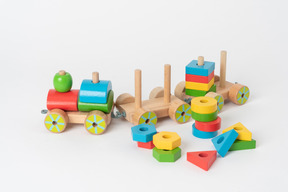 A colorful wooden toy train and geometrical shapes of many colors, lying against a plain white background