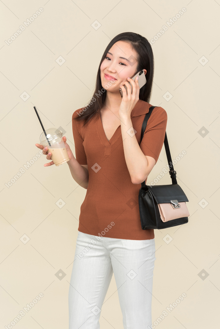 Улыбающаяся молодая азиатская девушка разговаривает по телефону