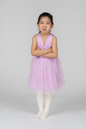 Petite fille en robe rose debout déçue avec ses bras croisés