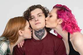 Парня с татуировкой целуют две девушки-подростки