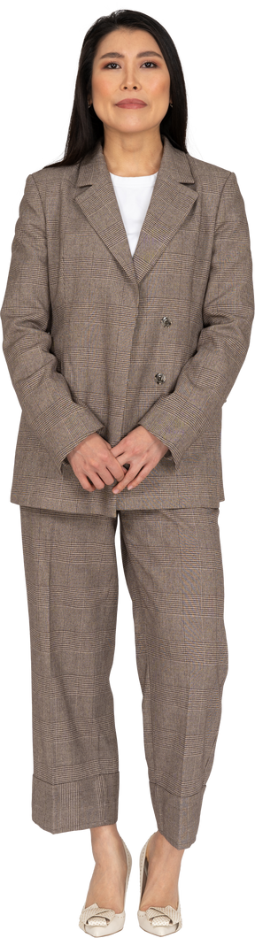 Front view of a confused young lady in brown business suit holding hands together