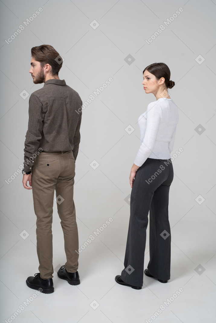 Vista posterior de tres cuartos de una pareja joven en ropa de oficina de pie todavía