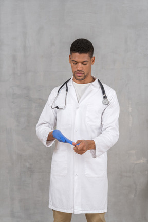 Young male doctor taking off medical gloves