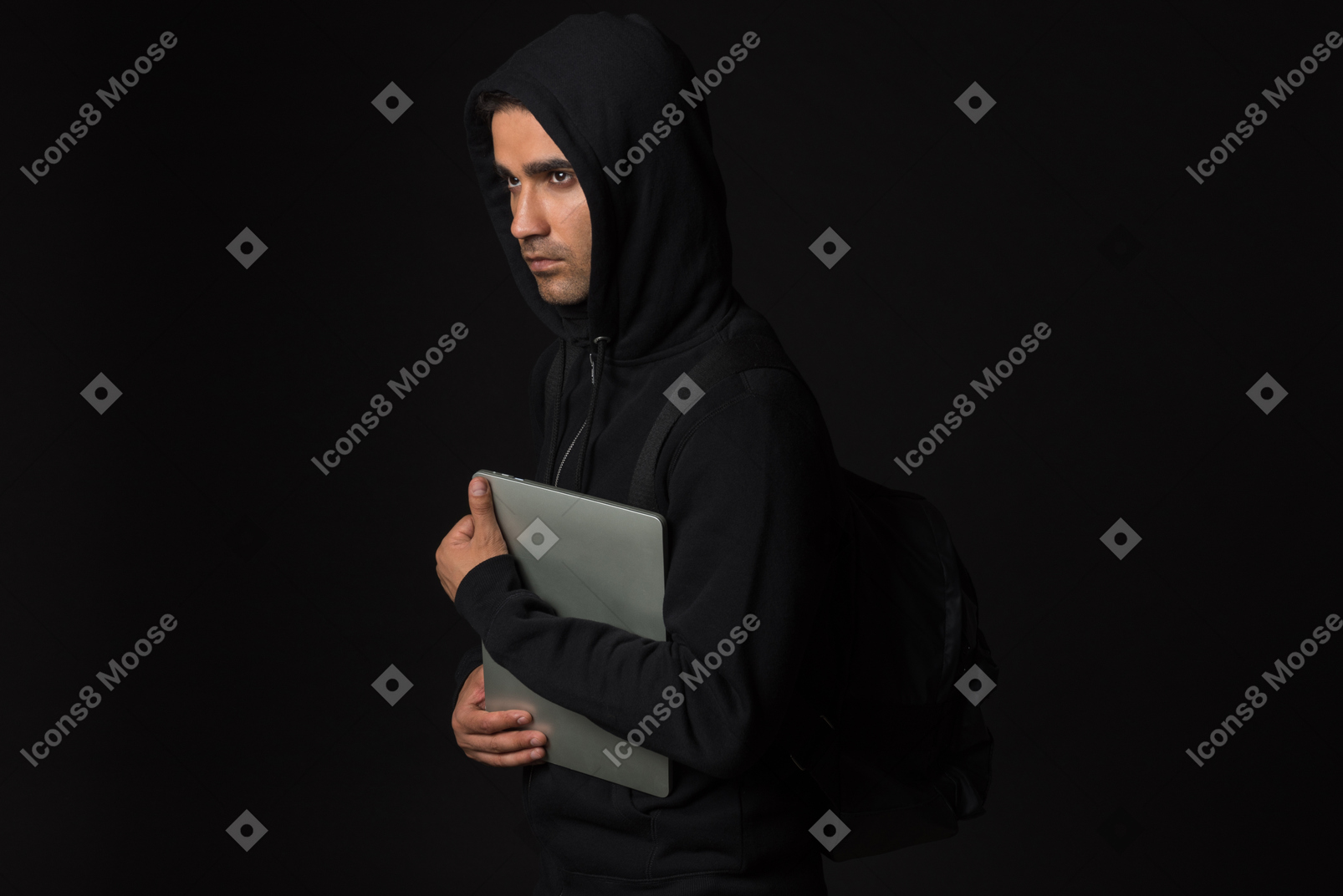 Chico hacker de pie en la oscuridad y sosteniendo portátil