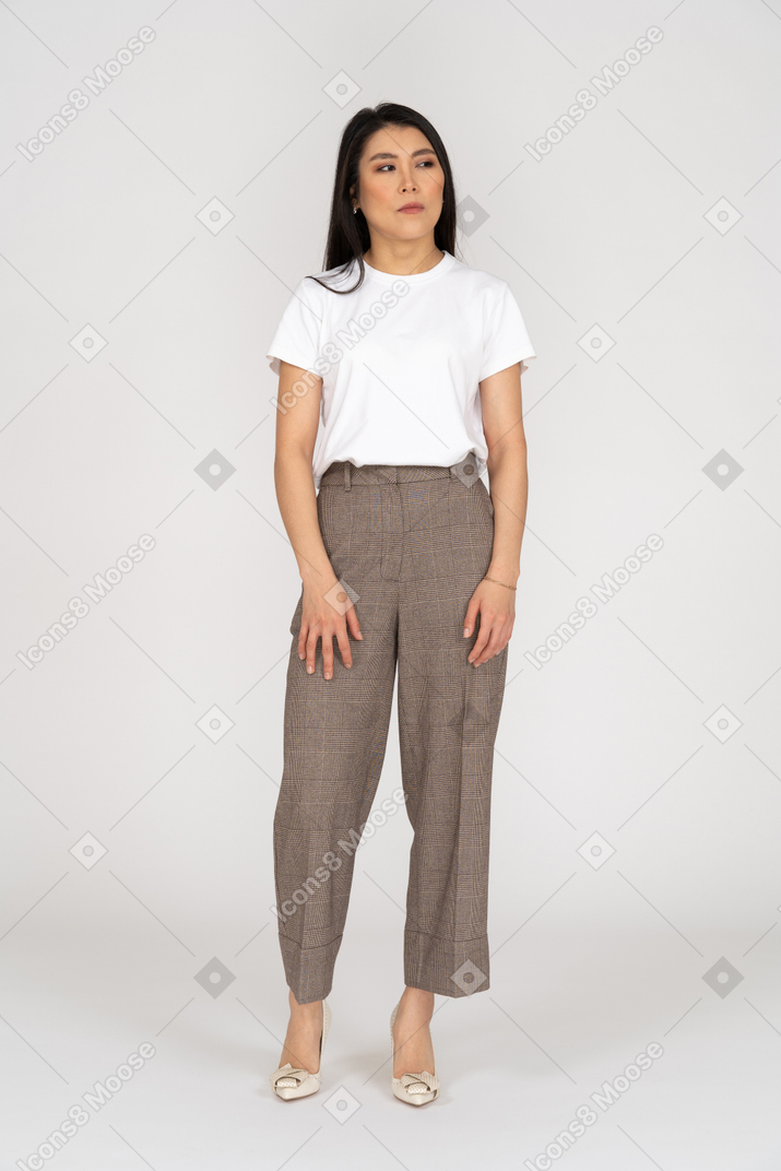 Vista frontale di una giovane donna sospettosa in calzoni e t-shirt che osserva da parte