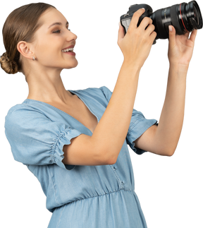 Vista di tre quarti di una giovane donna sorridente in abito blu che scatta una foto