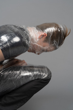 Jeune homme à genoux enveloppé dans du plastique