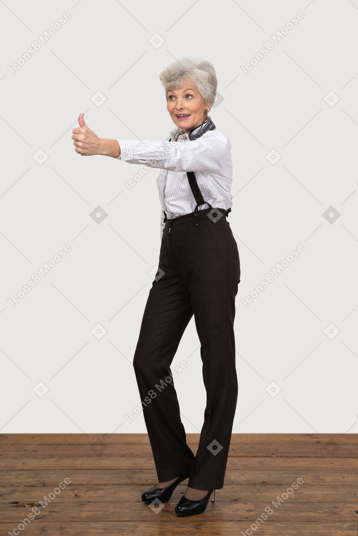 Vue de trois quarts d'une vieille dame en vêtements de bureau mettant le pouce vers le haut