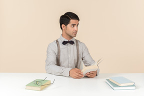 Jovem professor sentado à mesa e ler um livro