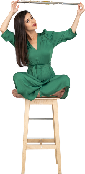 Девушка в полный рост, держащая кларнет над головой, сидя на деревянном стуле