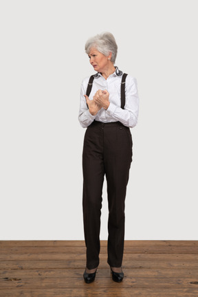 Front view of a crying old lady in office clothing holding hands together