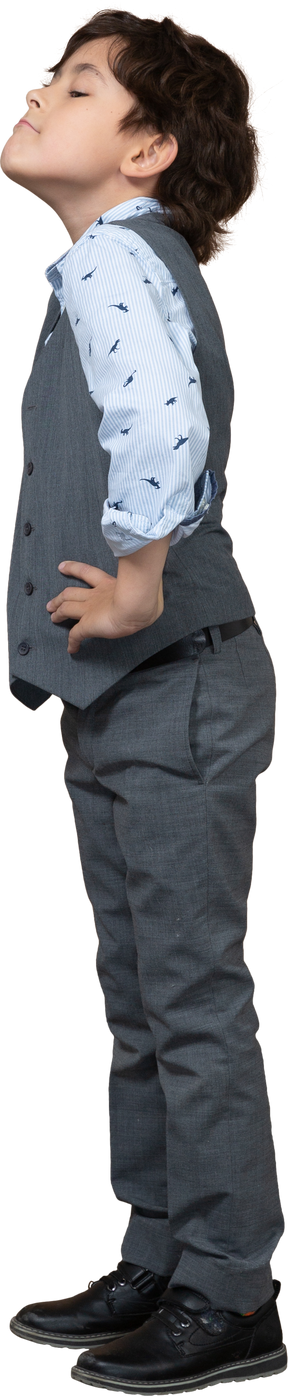 엉덩이에 손으로 포즈를 취하는 회색 양복에 귀여운 소년의 측면보기