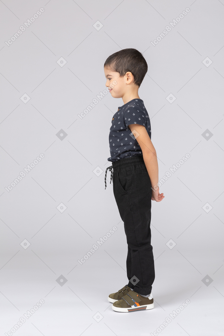 一个害羞的男孩穿着休闲服站在背后，双手往后看的侧视图