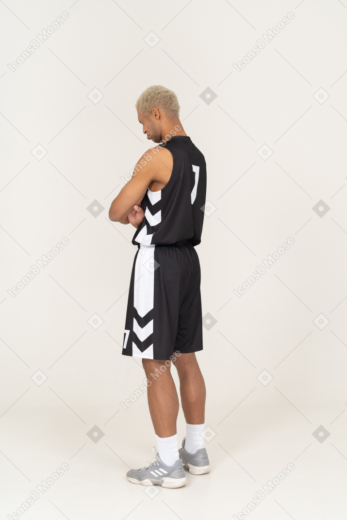 一个退缩的年轻男篮球运动员交叉双臂的四分之三后视图