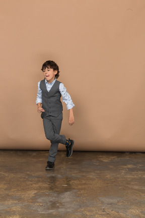 Vista frontal de um menino de terno cinza em pé com as pernas cruzadas