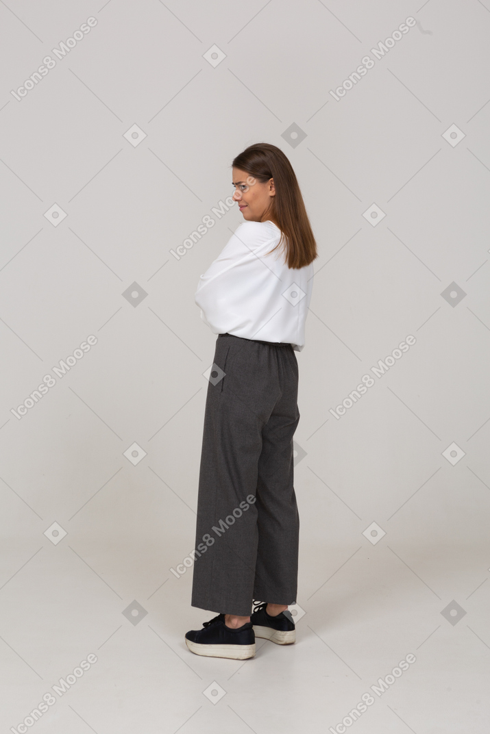 Vista posterior de tres cuartos de una joven disgustada en ropa de oficina cruzando los brazos