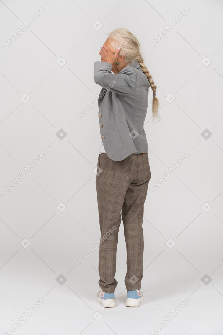 Rear view of an old lady in suit covering eyes with hands