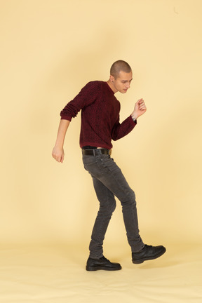 跳舞的年轻男子，穿着红色套头衫抬高腿的侧视图