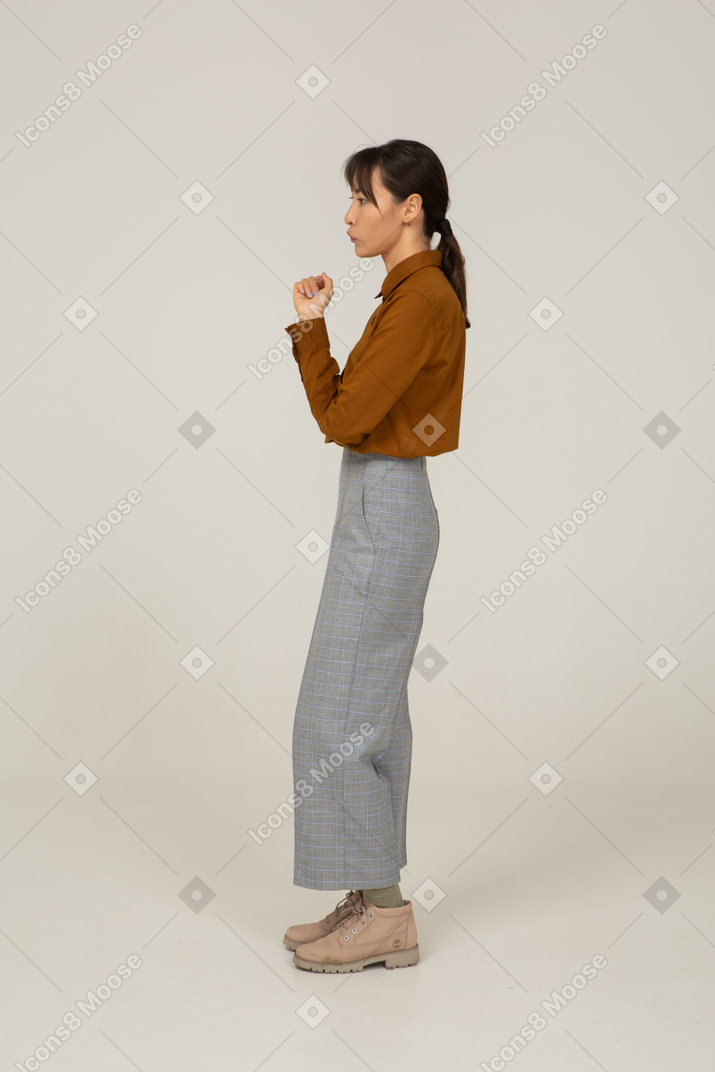 Side view of a guessing young asian female in breeches and blouse raising hand