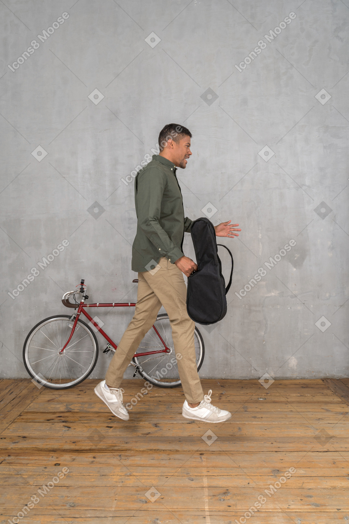 Side view of a man with a ukulele case jumping up