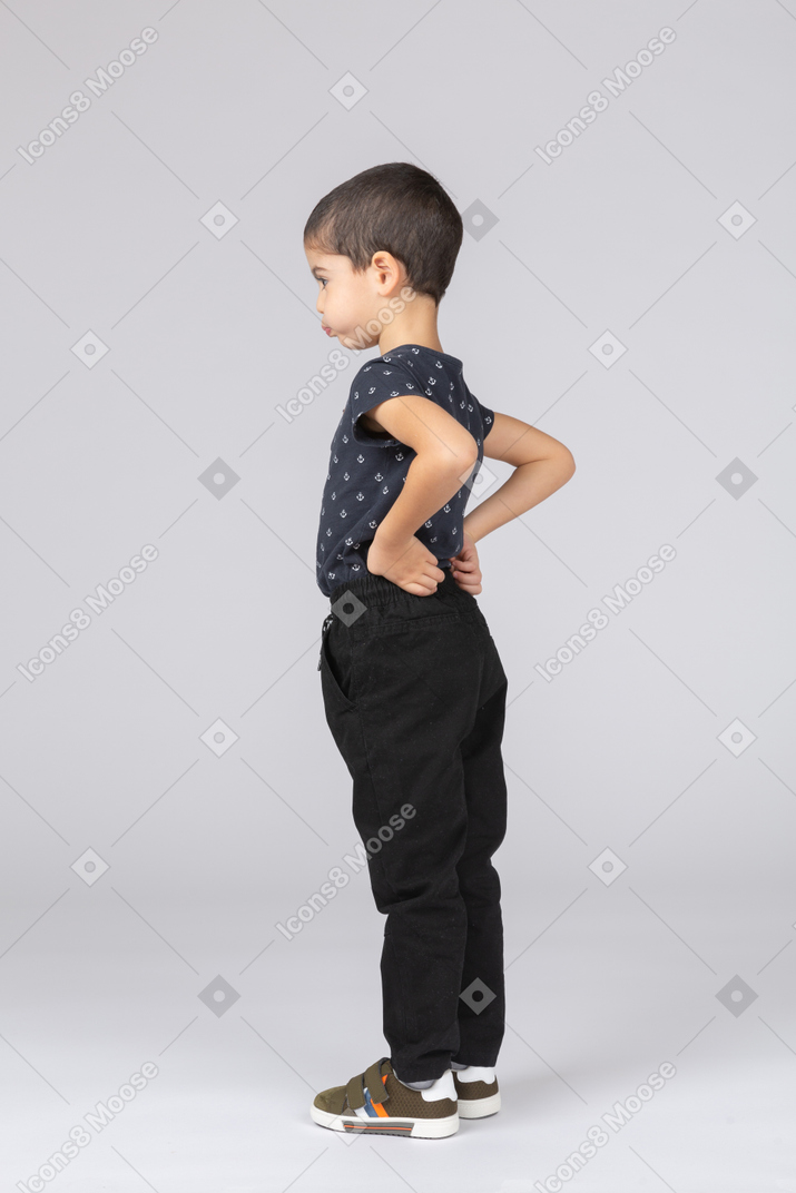 Side view of a cute boy in casual clothes posing with hand on back and making faces