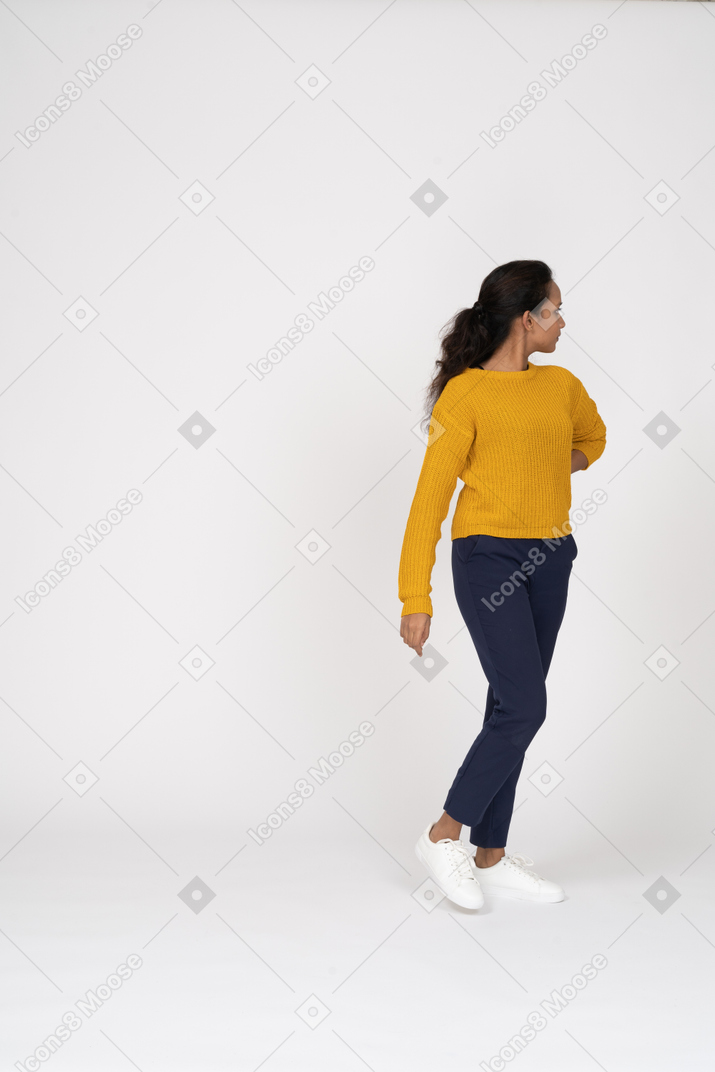 Front view of a girl in casual clothes standing with hand behing back and looking back