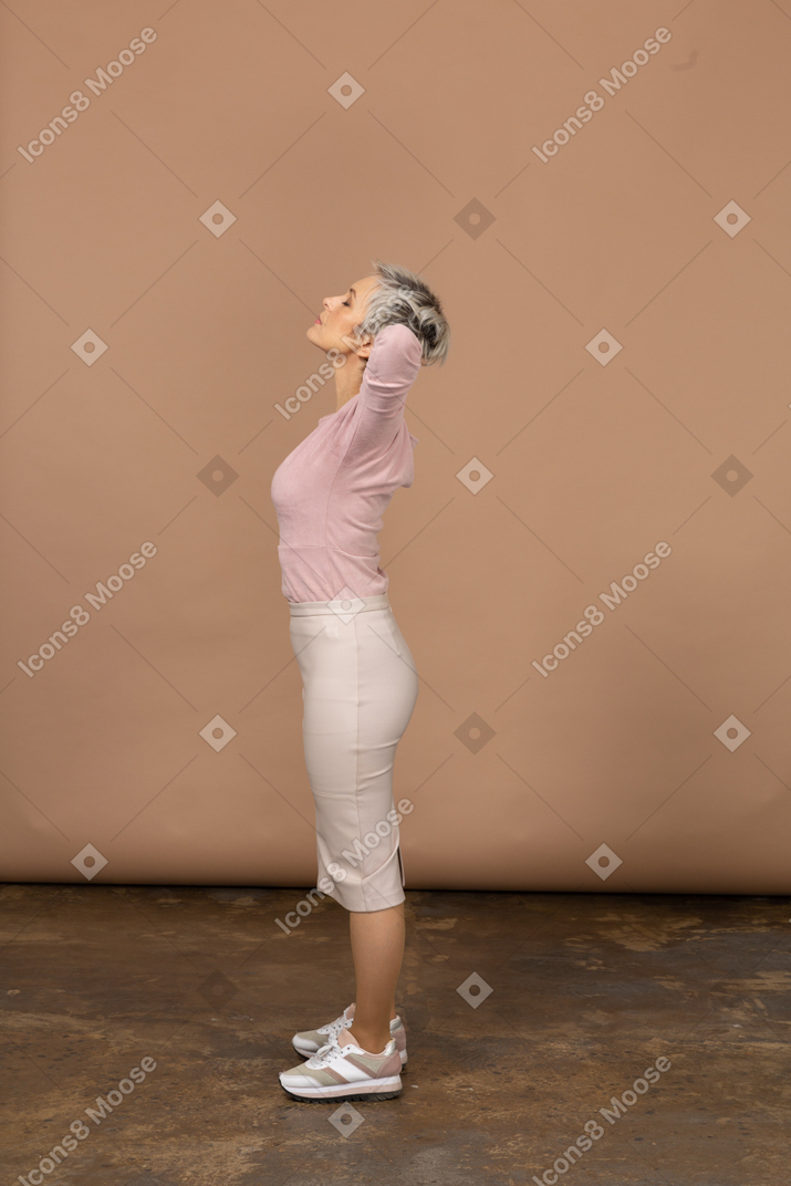 頭の後ろに手を置いて立っているカジュアルな服装の女性の側面図