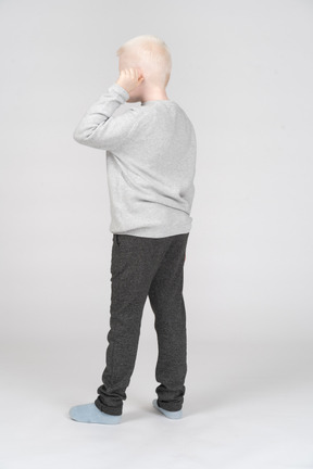 Three-quarter back view of a boy touching his ear