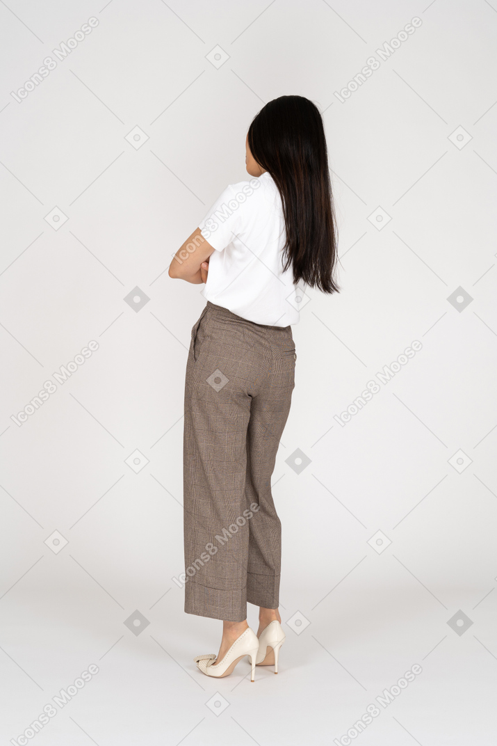 Three-quarter back view of a suspicious young lady in breeches and t-shirt crossing hands tilting head