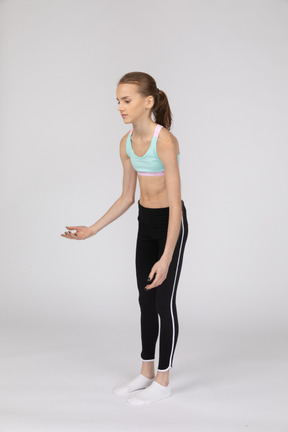 Вид в три четверти слабой девушки-подростка в спортивной одежде, наклонившейся вперед и жестикулирующей