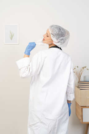 Back view of a young female doctor trying to take mask off