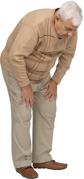 Vista laterale di un vecchio in abiti casual che si china e si tocca il ginocchio dolorante