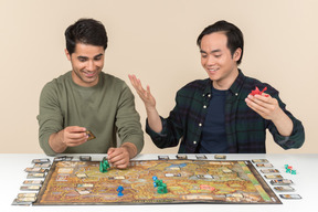 Interracial male friends sitting at the table and playing board game