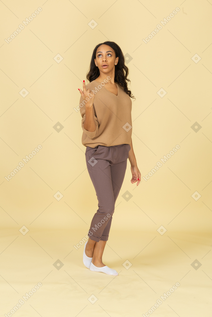 Vista de três quartos de uma jovem mulher de pele escura apontando o dedo para cima