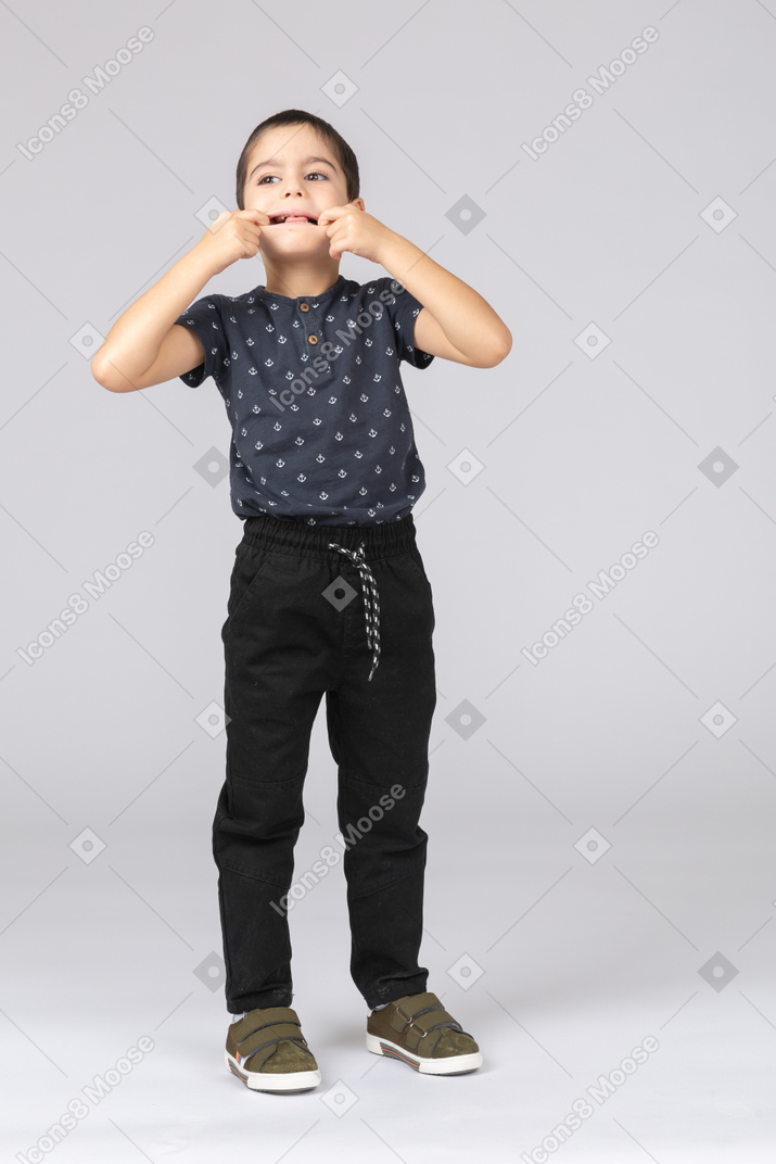 Front view of a cute boy opening mouth with fingers and looking up