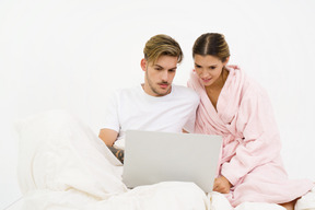 Pareja sentada en la cama y mirando portátil