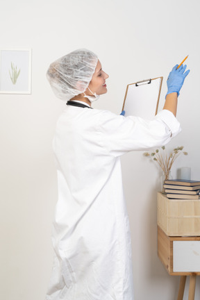 Three-quarter back view of a young female doctor holding pencil and tablet