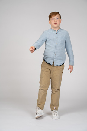 Vista frontal de um menino de pé com o braço estendido e olhando para a câmera
